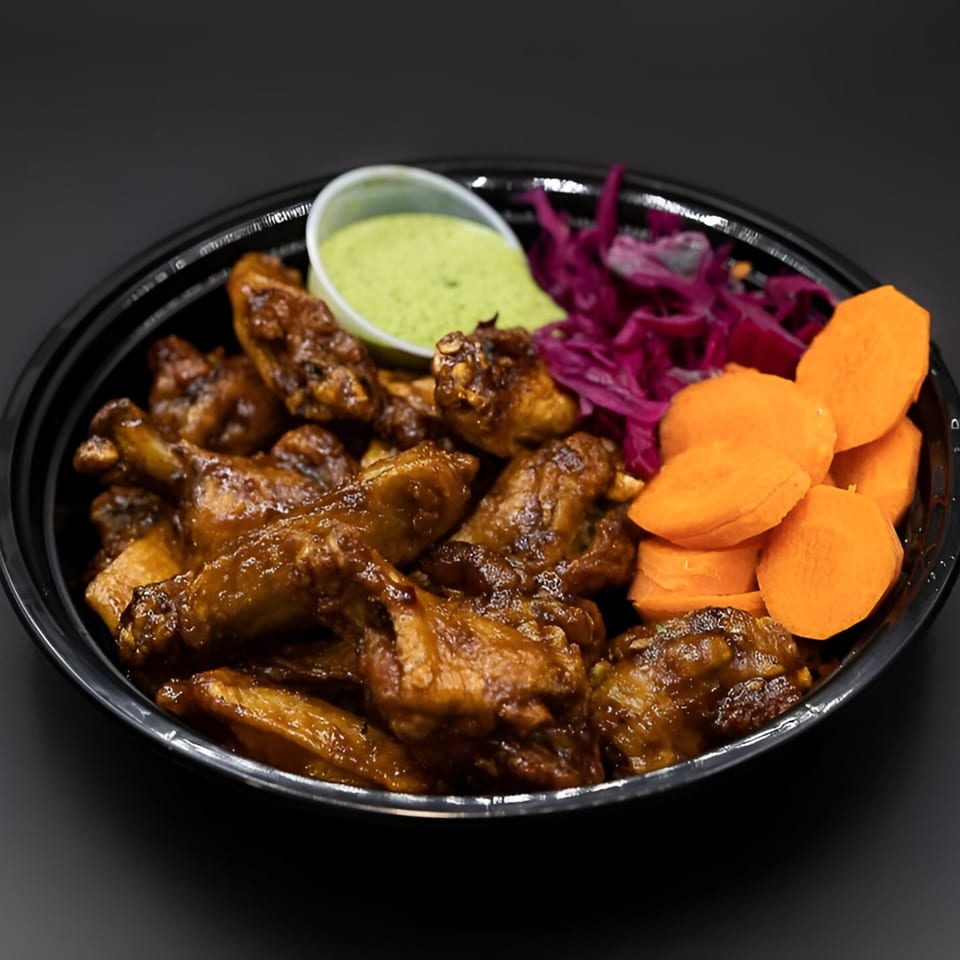 PhoGo Express chicken wings with green sauce, purple cabbage, and sliced carrots in a black bowl.