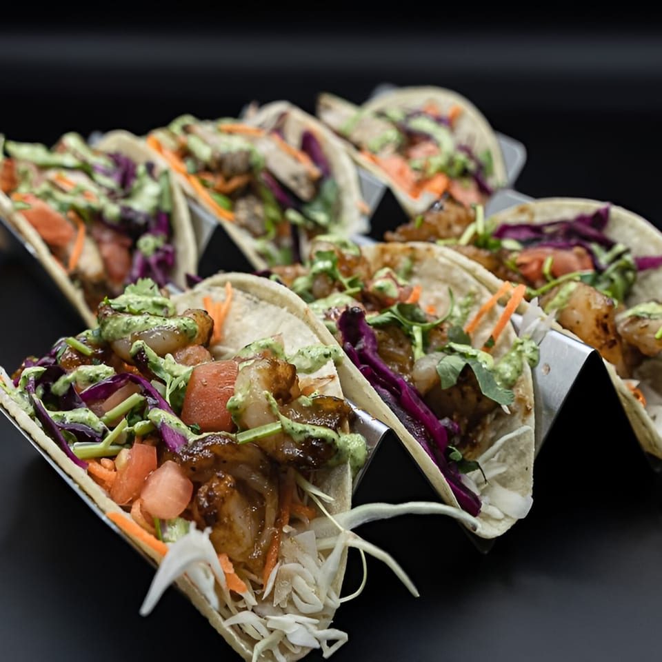 Multiple PhoGo Express Vietnamese tacos with shrimp, cabbage, and green sauce on a black background.