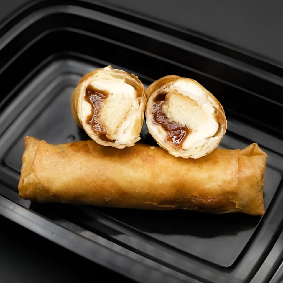 A golden-brown fried spring roll, with two halves of another showing a sweet banana and caramel filling.