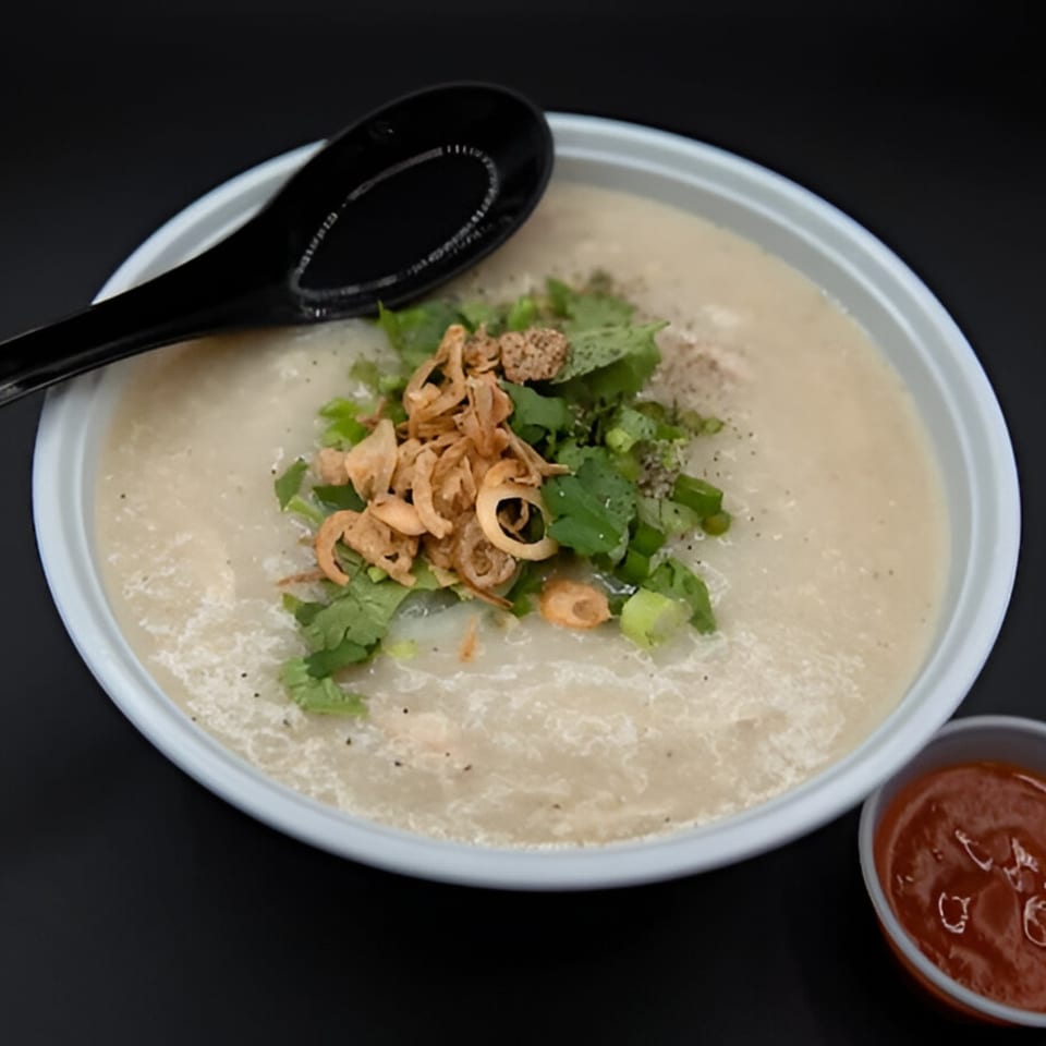 PhoGo Express congee topped with fried shallots, cilantro, and green onions, with a side of chili sauce.