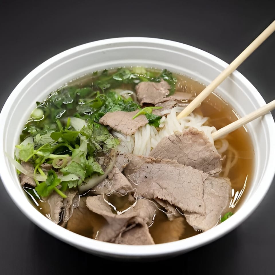 A white bowl of PhoGo Express pho with beef, noodles, and fresh herbs, with chopsticks.